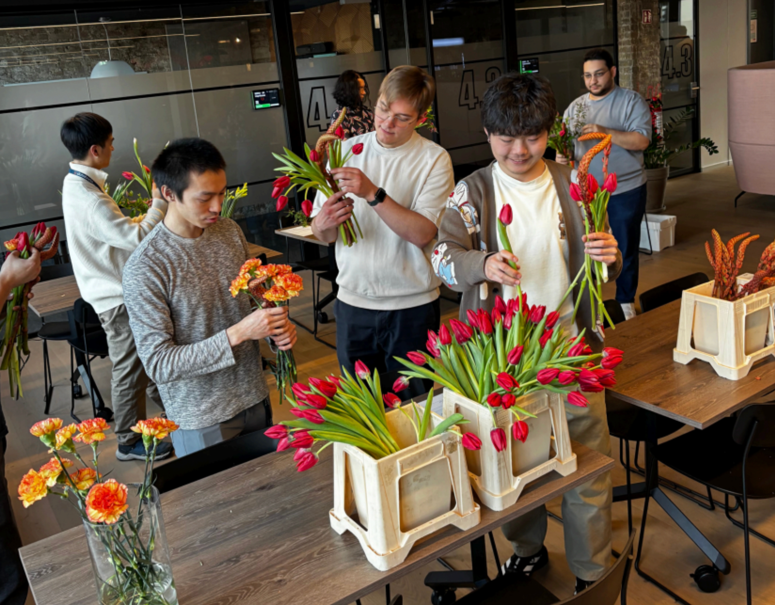 Group of people arranging tulips in crates in a room with tables and chairs.