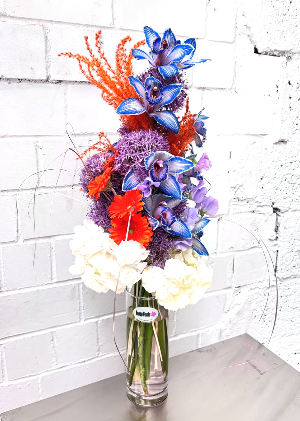 Bouquet of colorful flowers in a clear vase against a white brick wall.