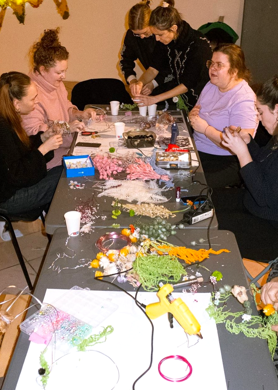 Group of people engaged in a craft activity around a table with various materials and tools.
