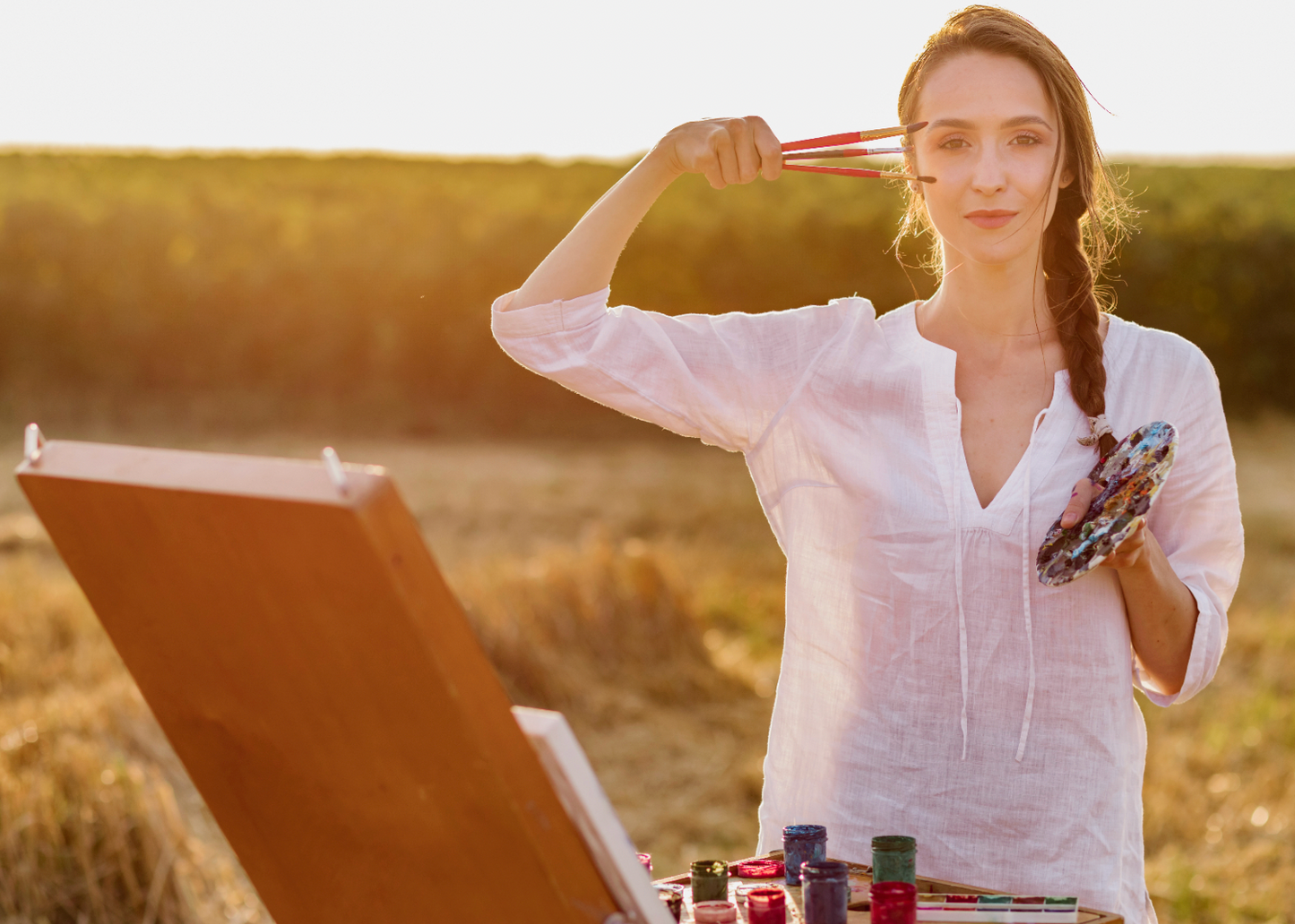 Woman painting outdoors in a field with an easel and paint supplies.