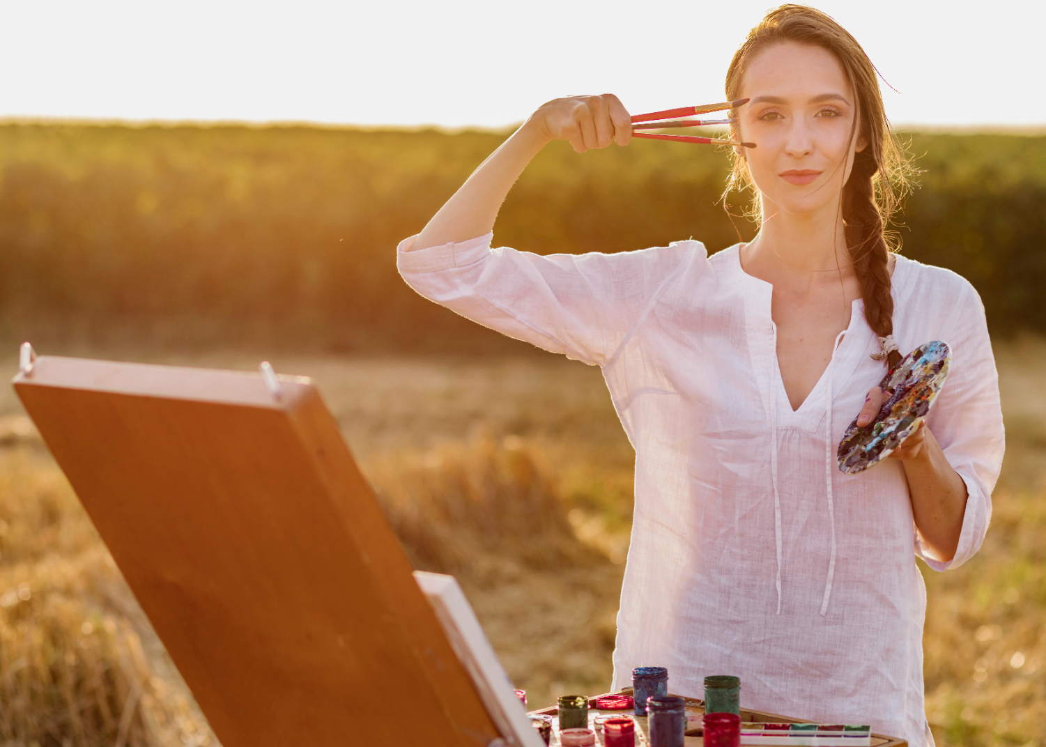 Woman painting outdoors in a field with an easel and paint supplies.