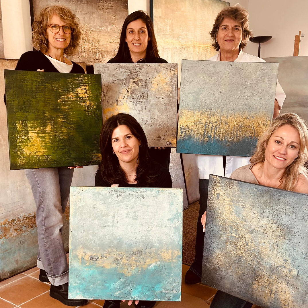 Five women holding and displaying abstract paintings in a room with a tiled floor.