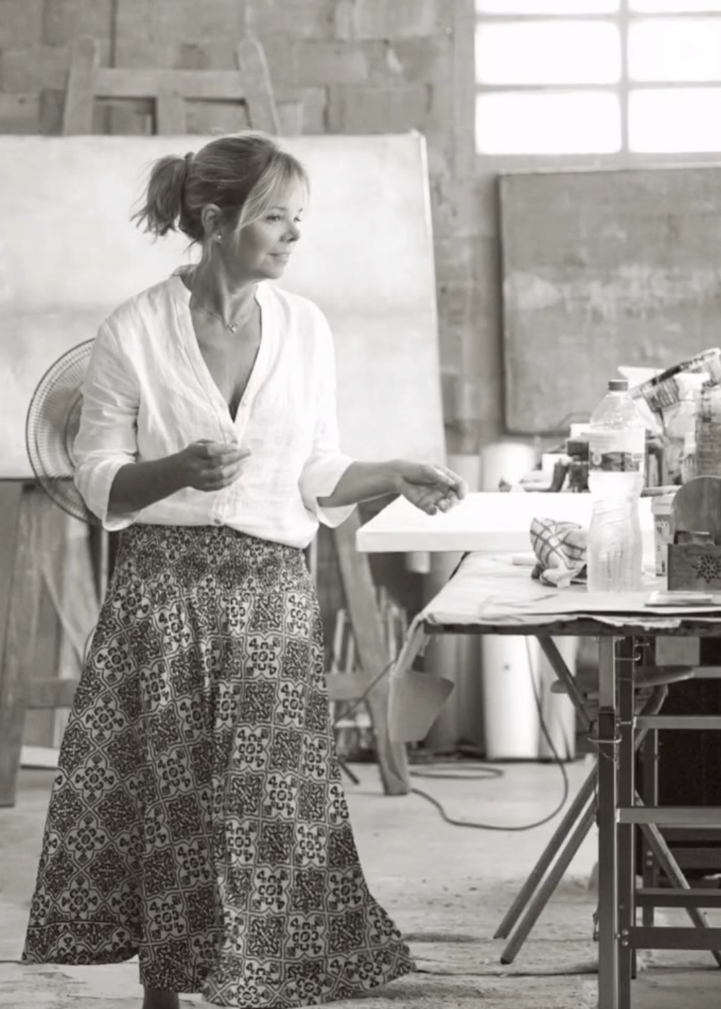 Woman standing in a studio with art supplies and a large canvas.