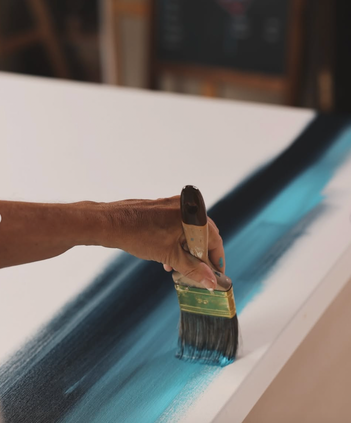 Hand painting a surface with a blue color using a paintbrush.
