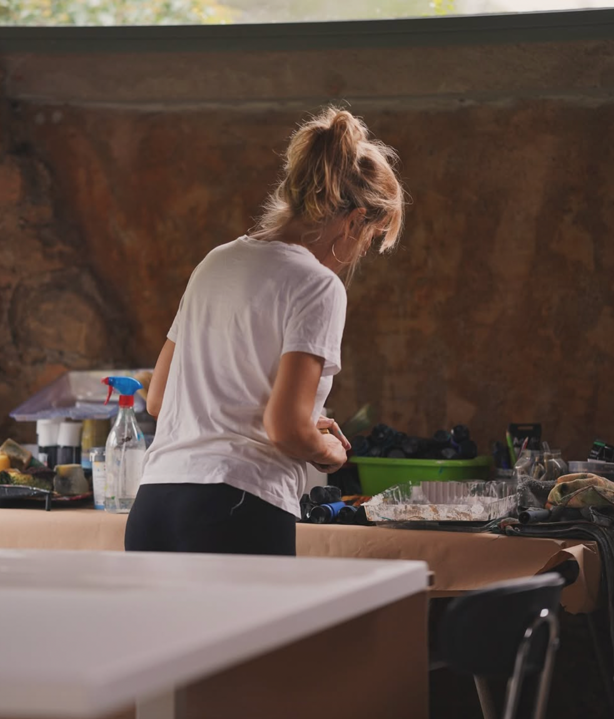 Person in a white shirt standing at a counter with various items around