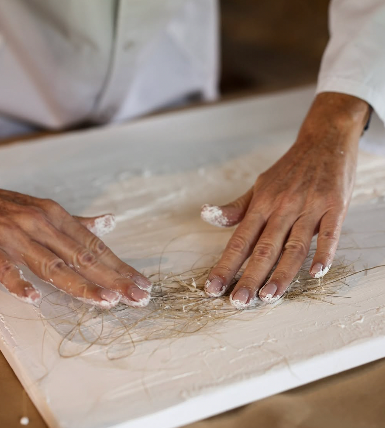 Hands working with materials on a flat surface, possibly in a workshop setting.