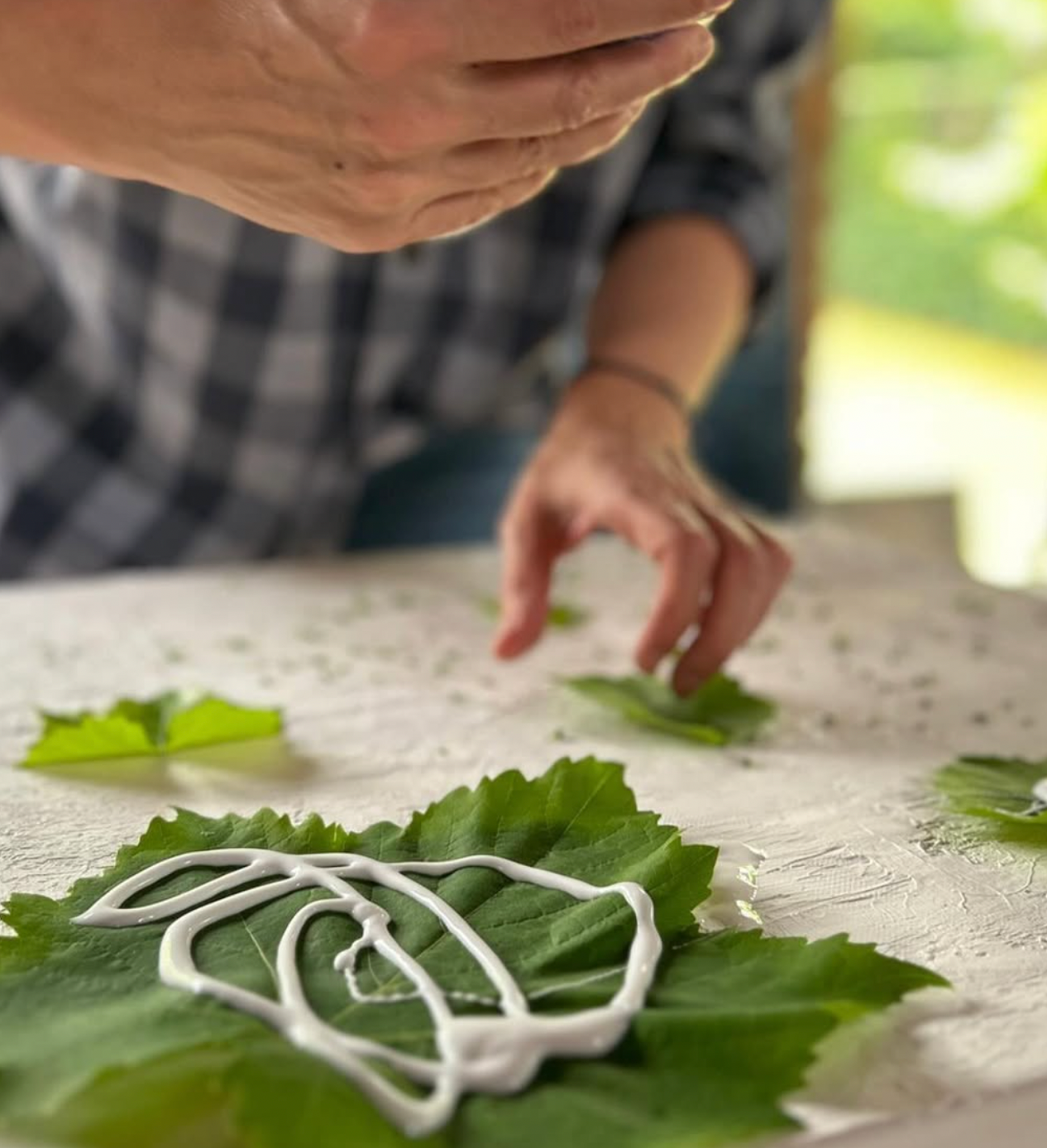 Person preparing food with green leaves and white sauce on a table.