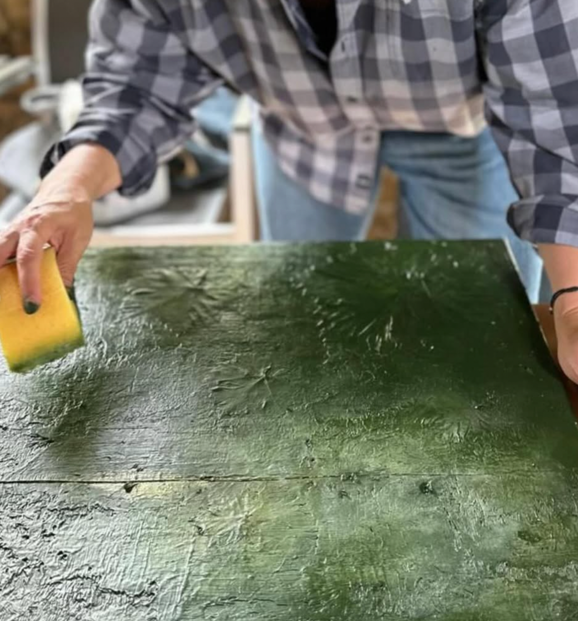 Person cleaning a green wooden surface with a sponge.
