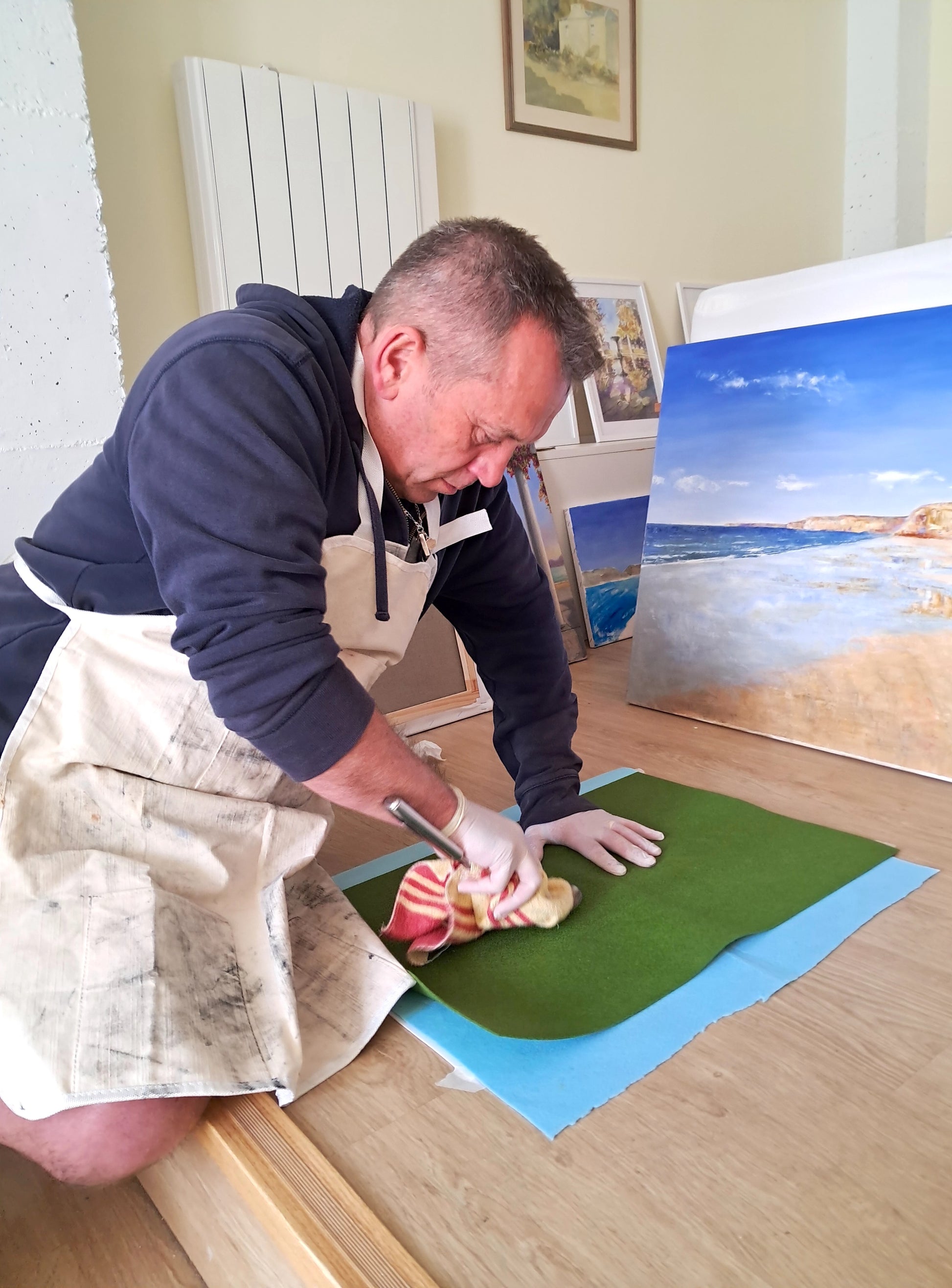 Man cleaning a painting with a cloth on a wooden floor