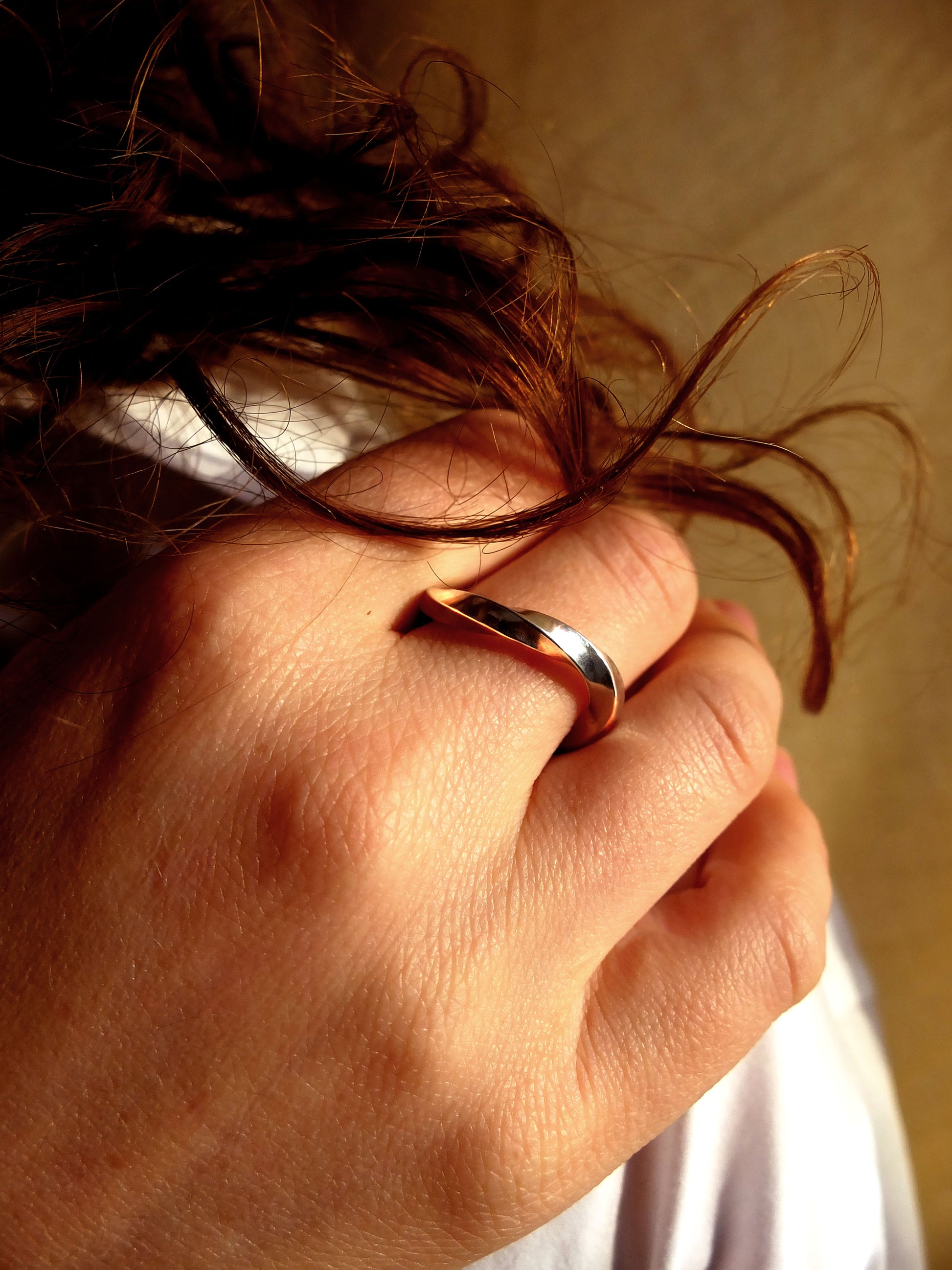 Hand with a silver ring holding hair against a neutral background
