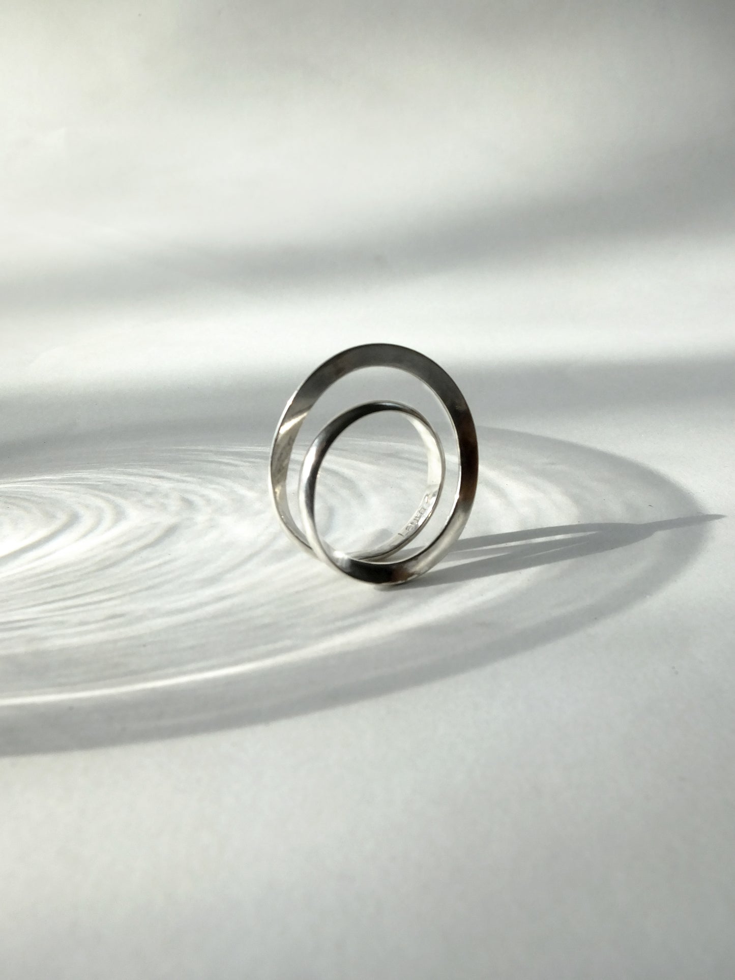 Silver ring on a reflective white surface with concentric circular patterns