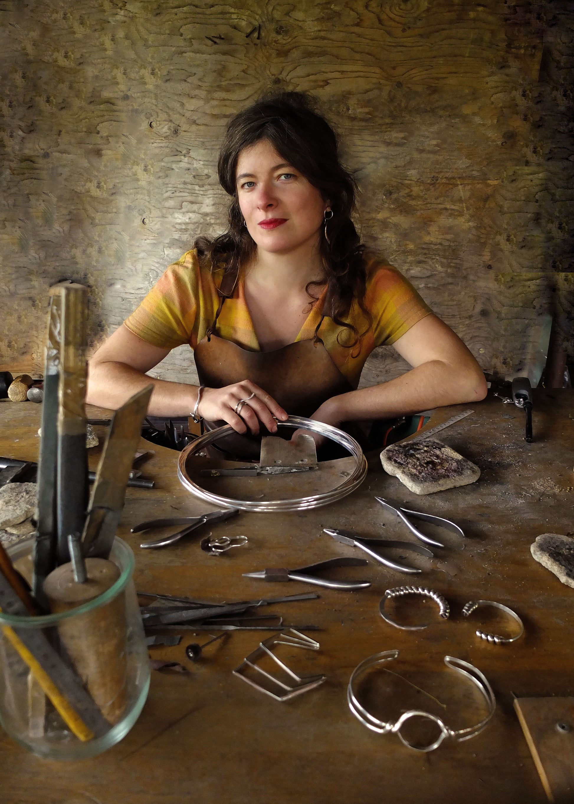 Woman working with metal jewelry at a table in a workshop.