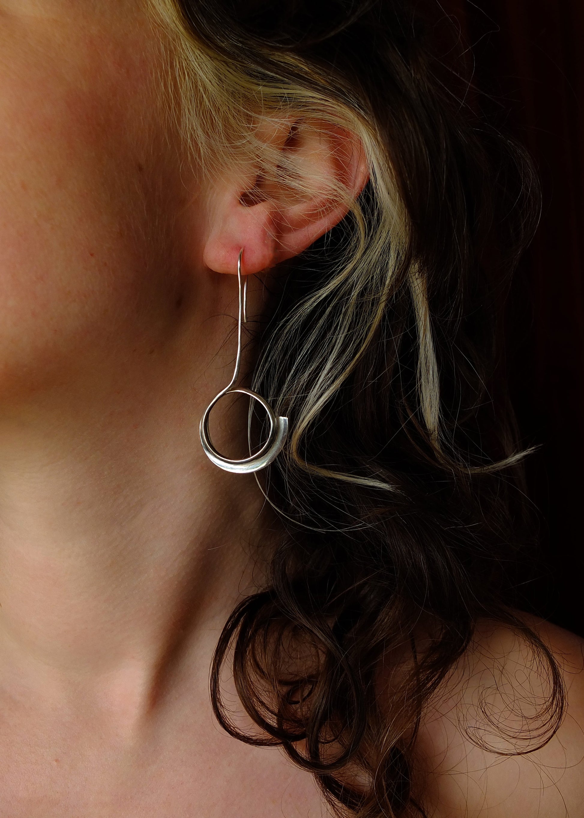 Close-up of a person wearing a silver hoop earring with a dark background