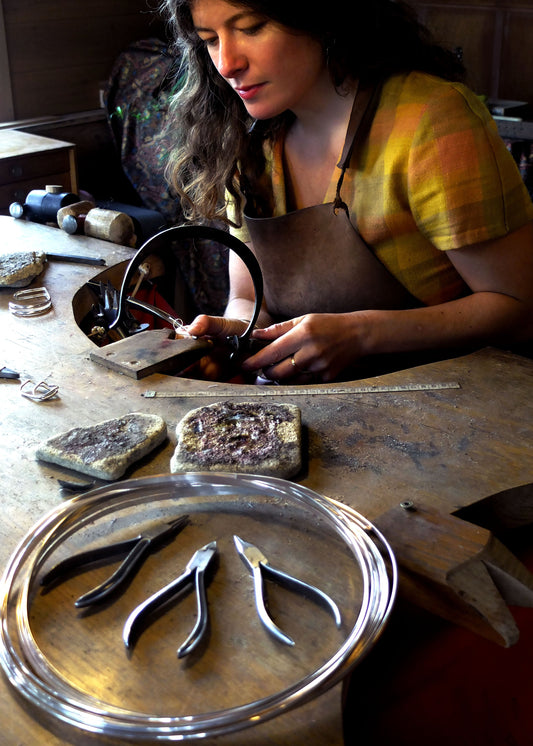 Person working with jewelry-making tools and materials on a table.