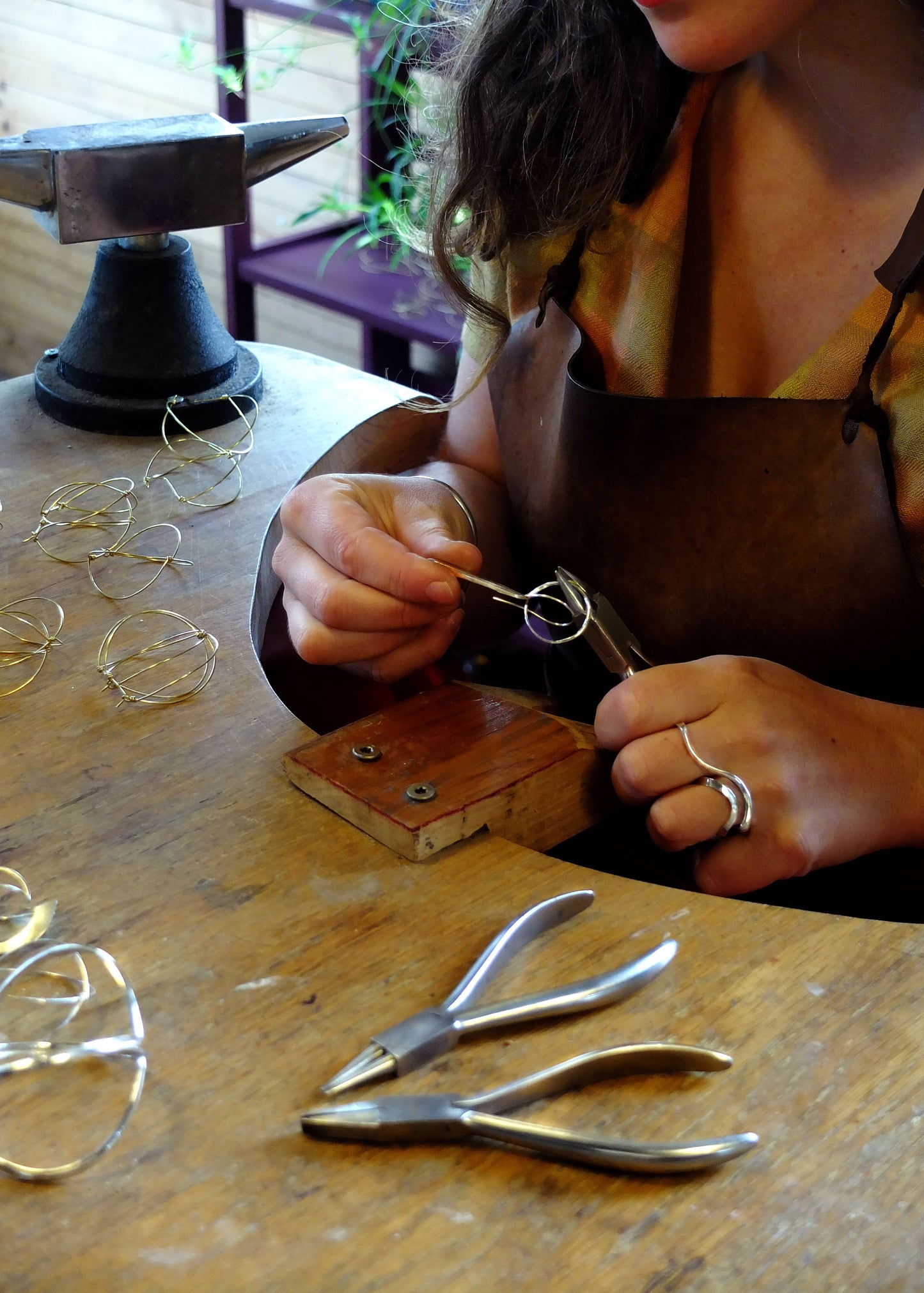 Person working with jewelry on a wooden table with tools and materials.