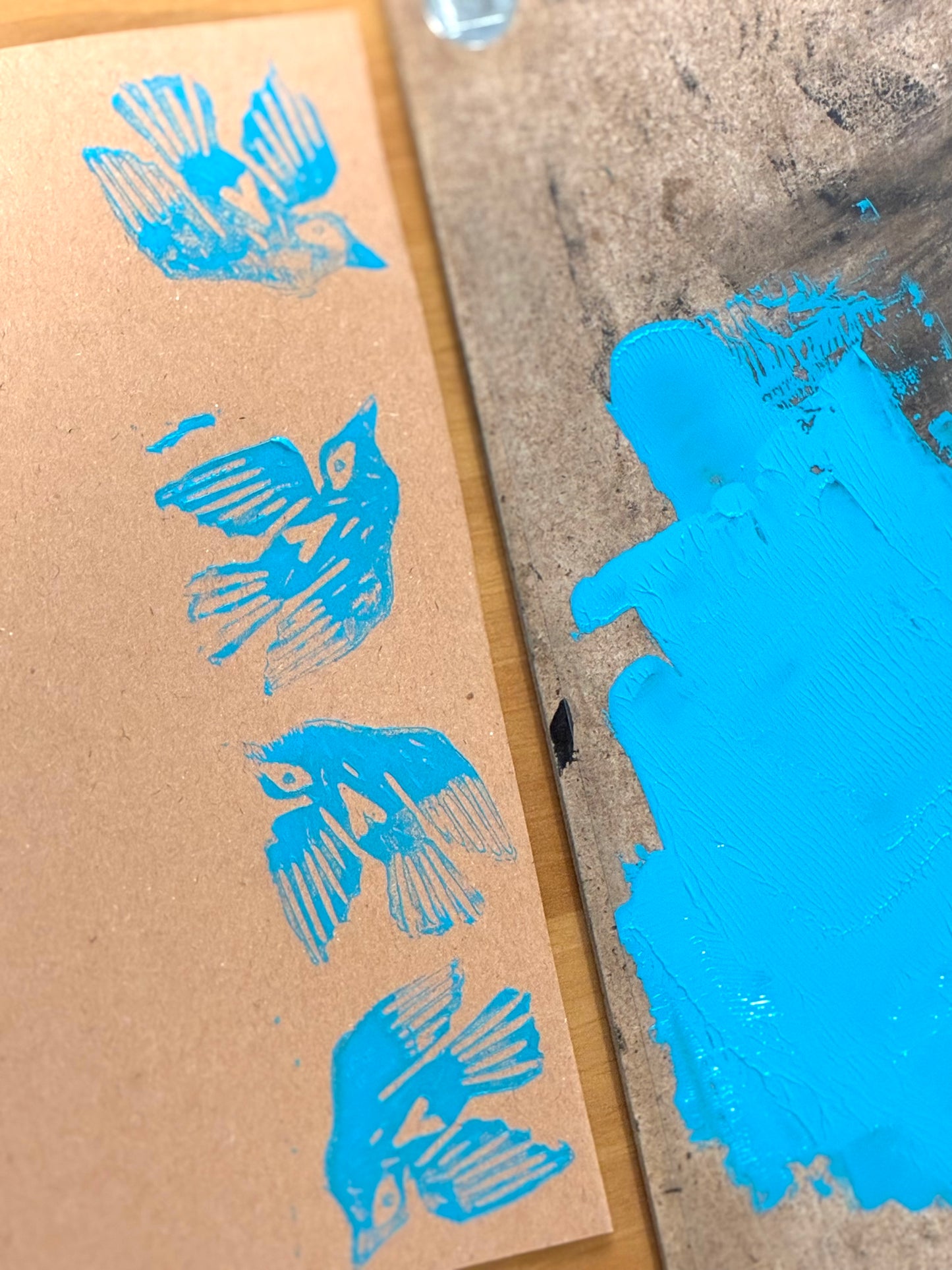 A close-up of a brown kraft paper card printed with four blue bird silhouettes, next to a textured surface with a bright blue paint smear.