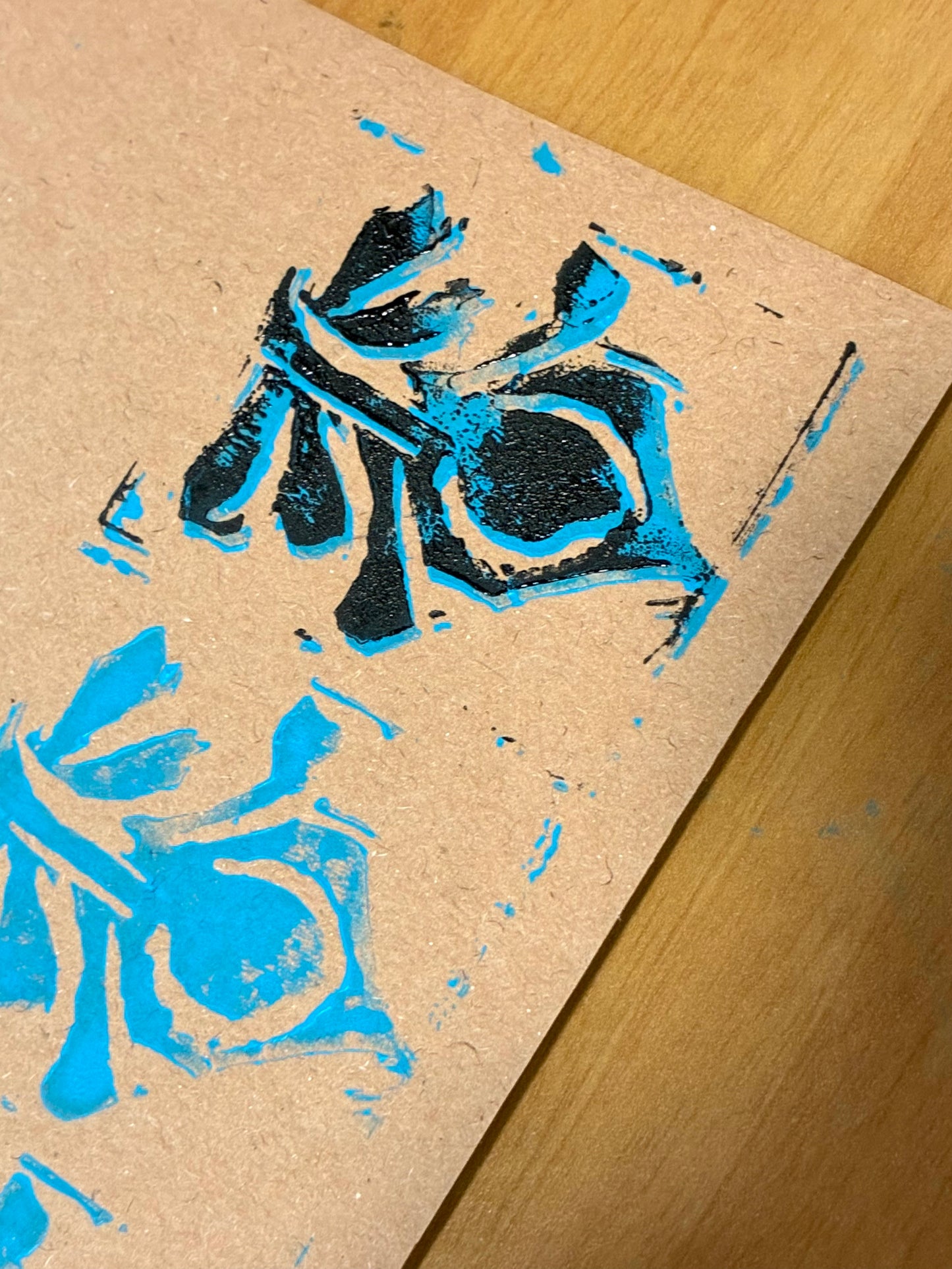 A close-up of a textured kraft paper sheet featuring a blue and black block-print style design, placed diagonally on a light brown wooden surface.