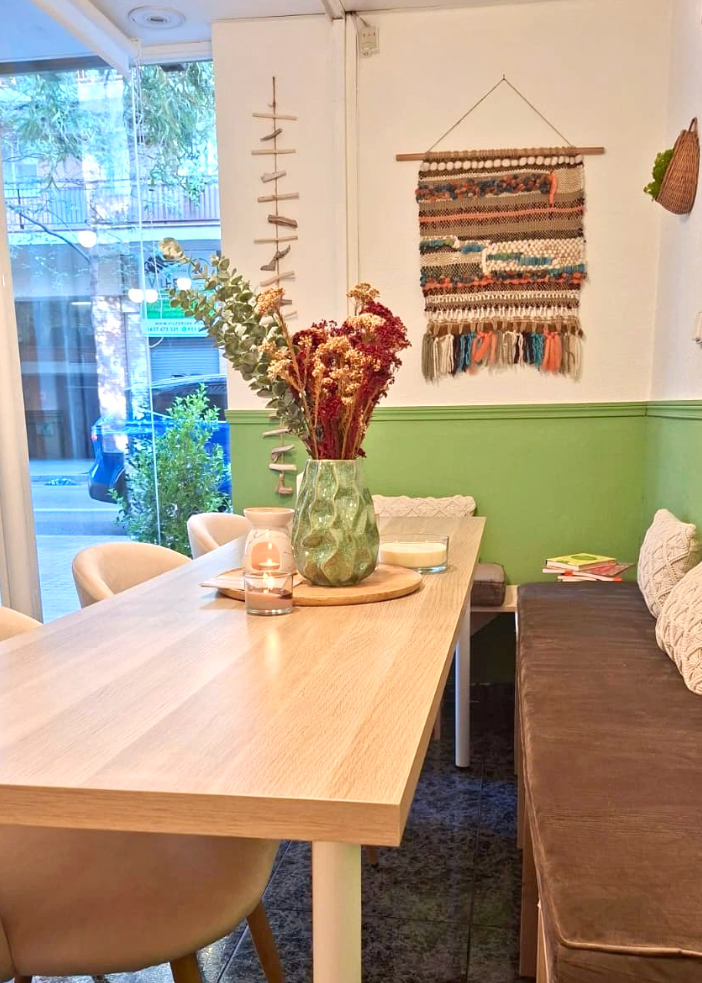 A modern dining area featuring a light wood table and chairs next to a wooden bench with a brown cushion, decorated with a green and white wainscoted wall and a bohemian wall hanging.