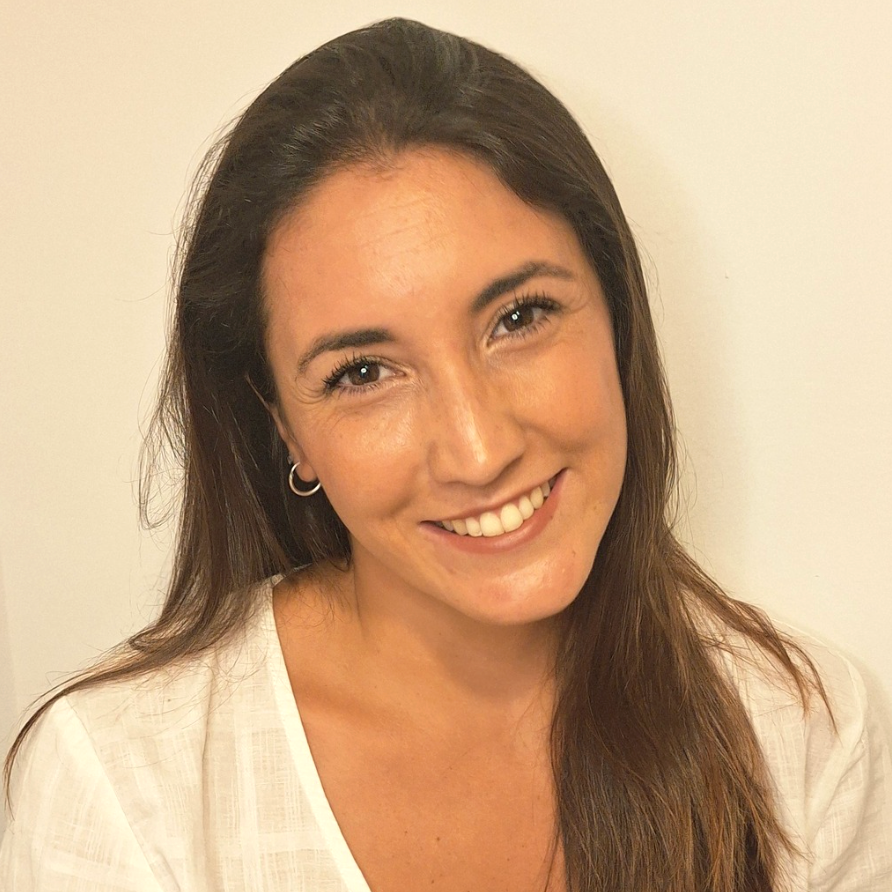 A smiling woman with long brown hair wearing a white textured top, photographed against a plain off-white background.