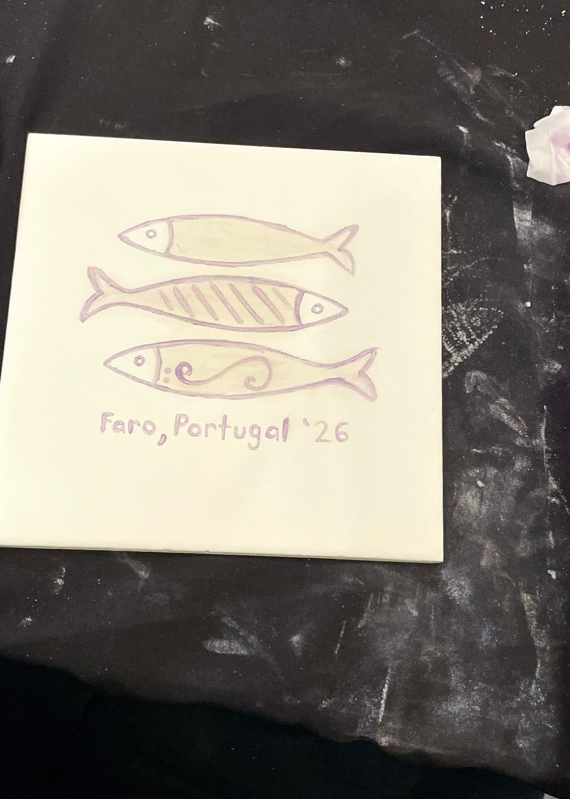 Note card with fish illustrations and 'Faro, Portugal '26' text on a dark surface