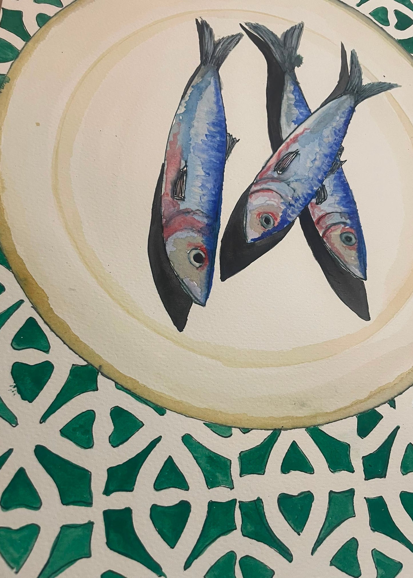 A circular ceramic plate with a hand-painted illustration of three blue and silver sardines, set against a green and white patterned tile background.