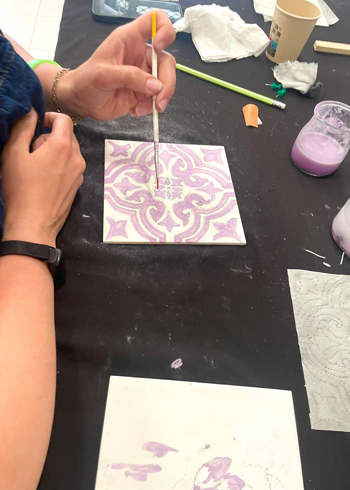 Person working on a craft project with a patterned tile and various tools on a black surface.