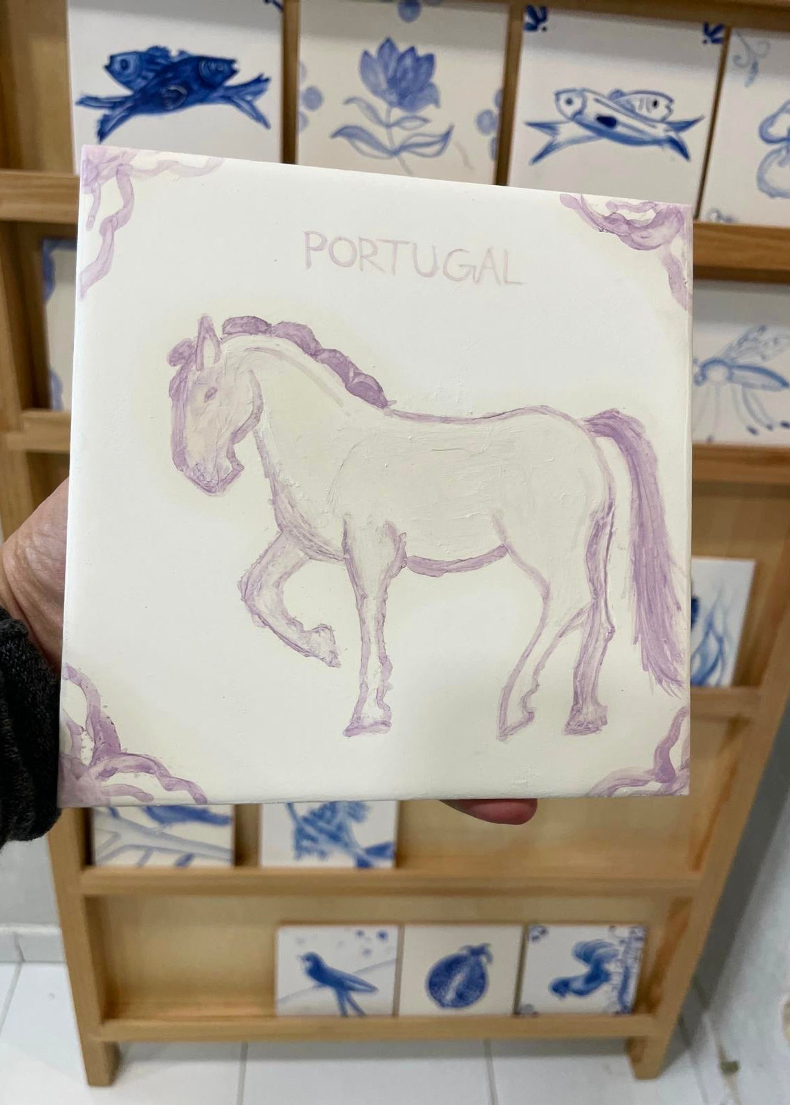 Card with a horse illustration and 'Portugal' text held in front of a decorative tile rack.