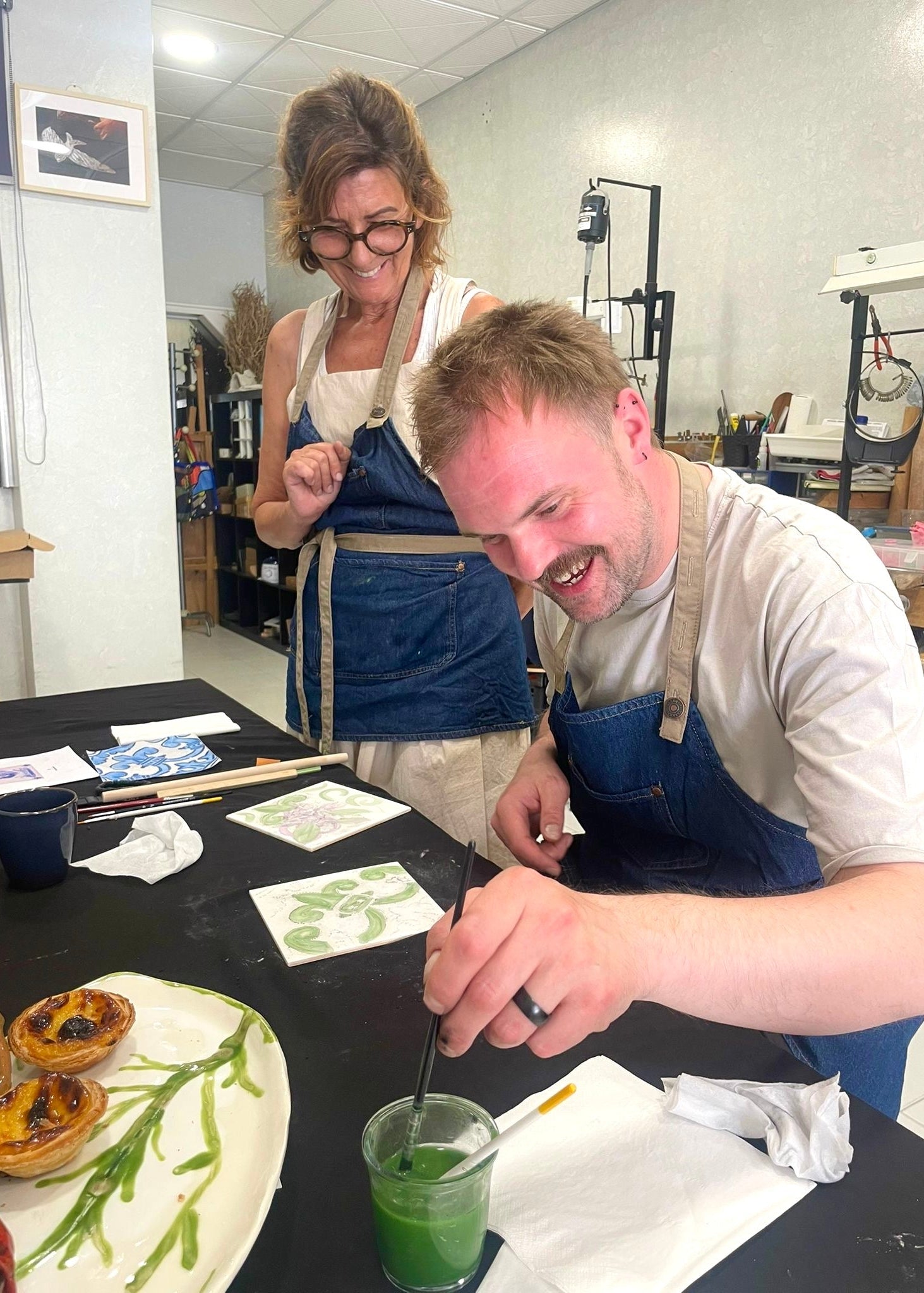 Two people in a kitchen setting, one holding a glass with a green liquid.