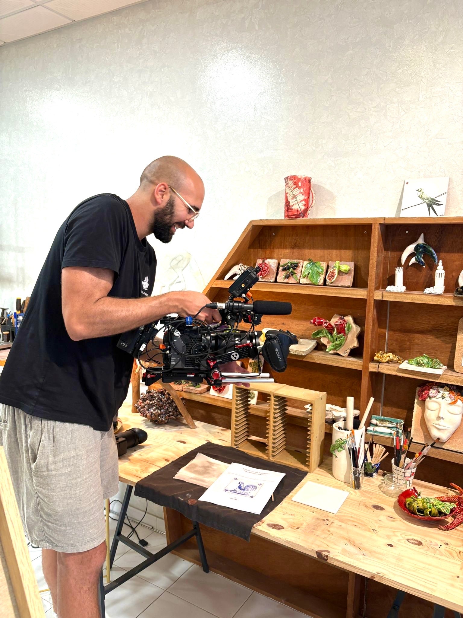 Man operating a camera in a room with shelves and a table.