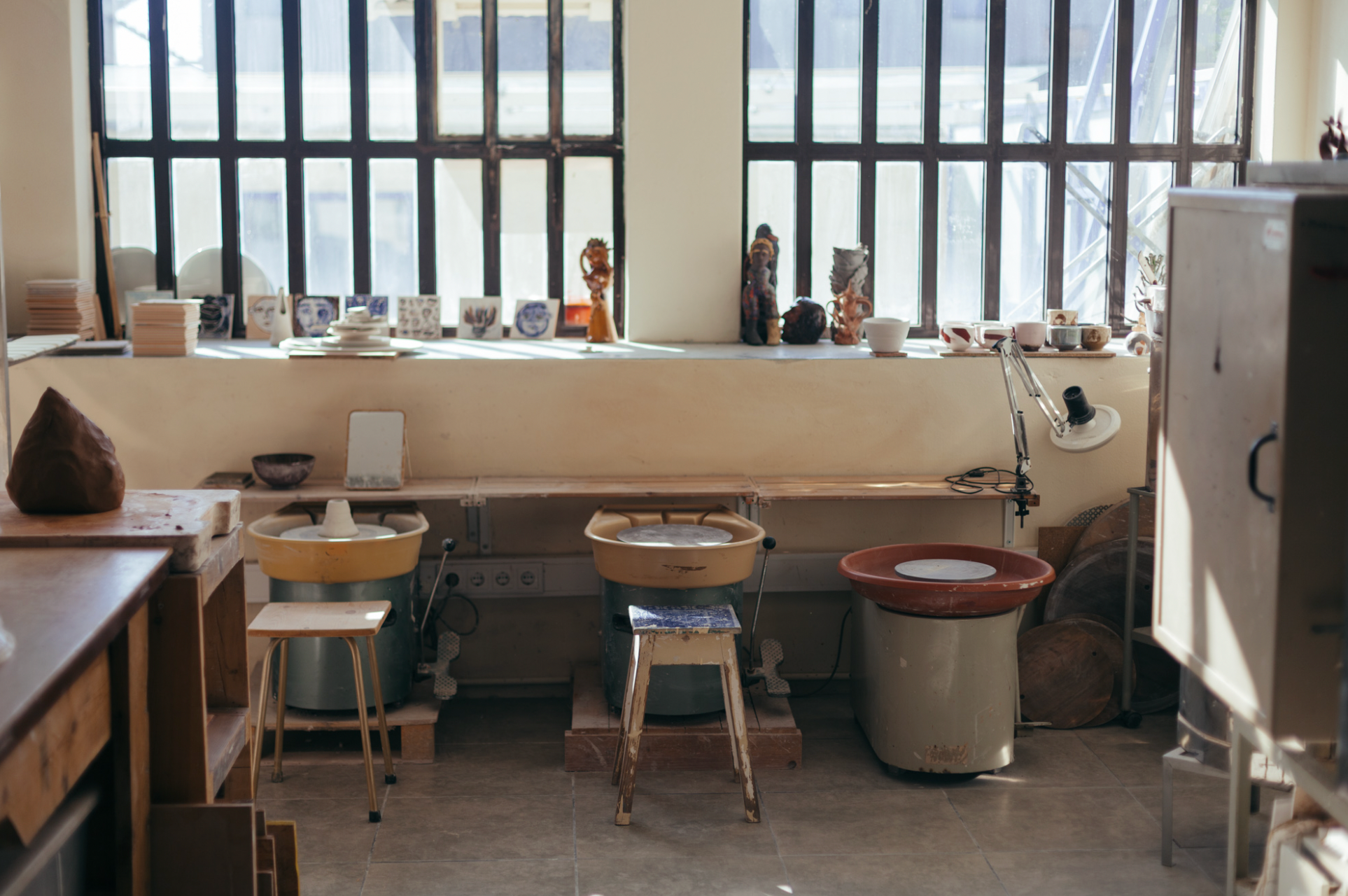 Studio with pottery items on a shelf and stools in front of large windows.