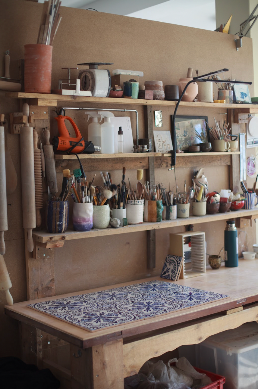 Art studio with shelves filled with painting supplies and a tiled table.