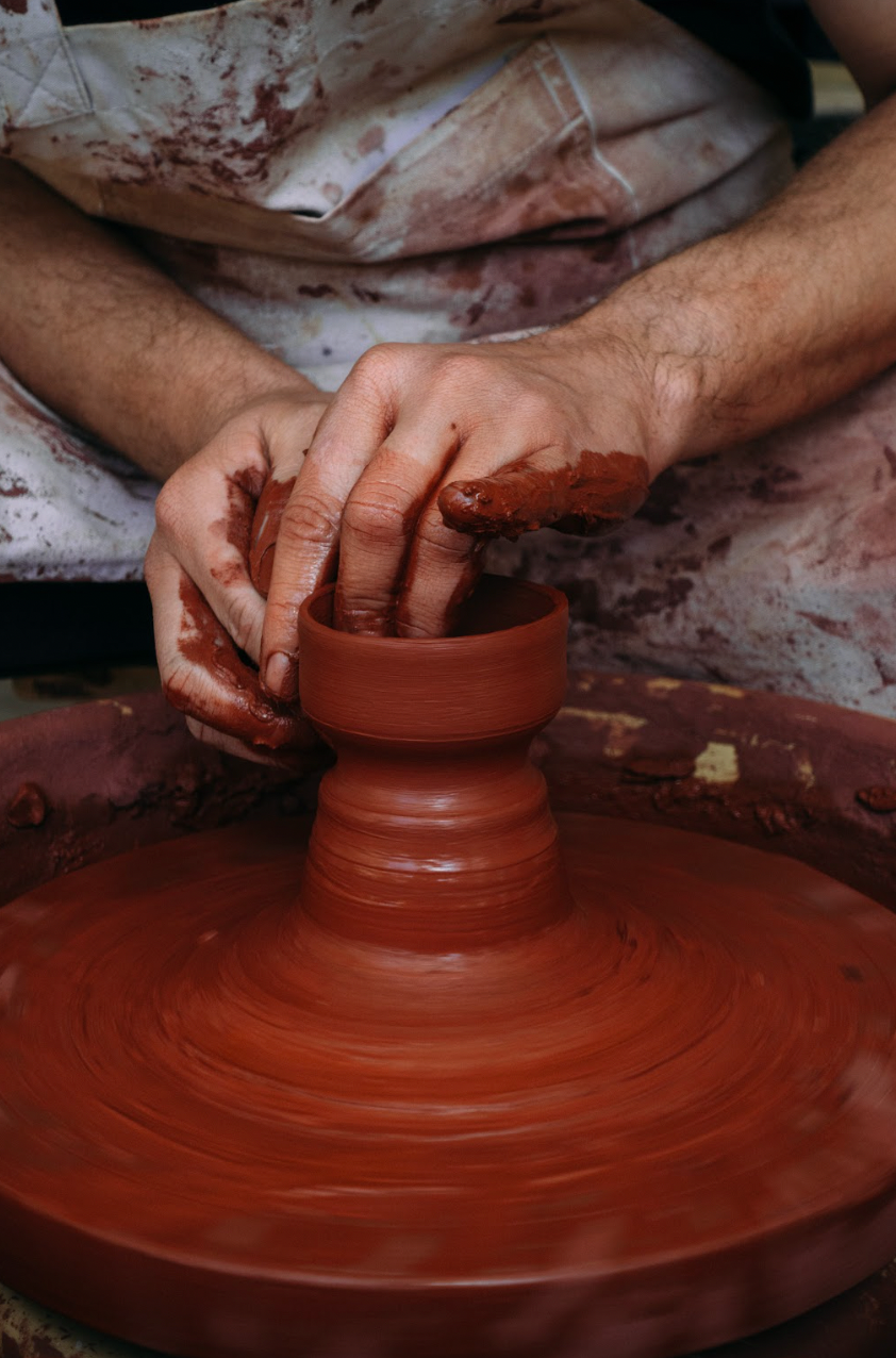 Person shaping a clay pot on a pottery wheel