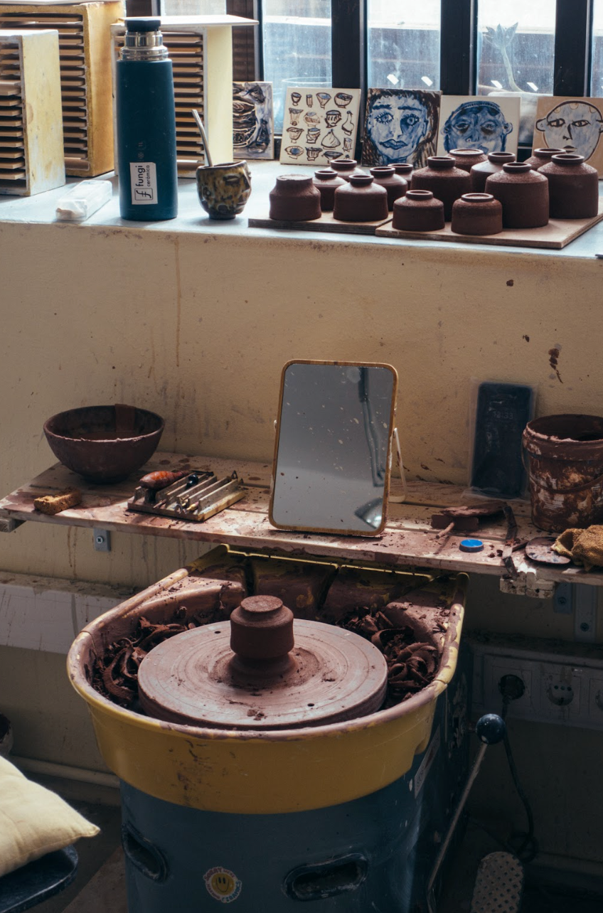 Workshop with pottery wheel, clay pots, and tools on a counter.