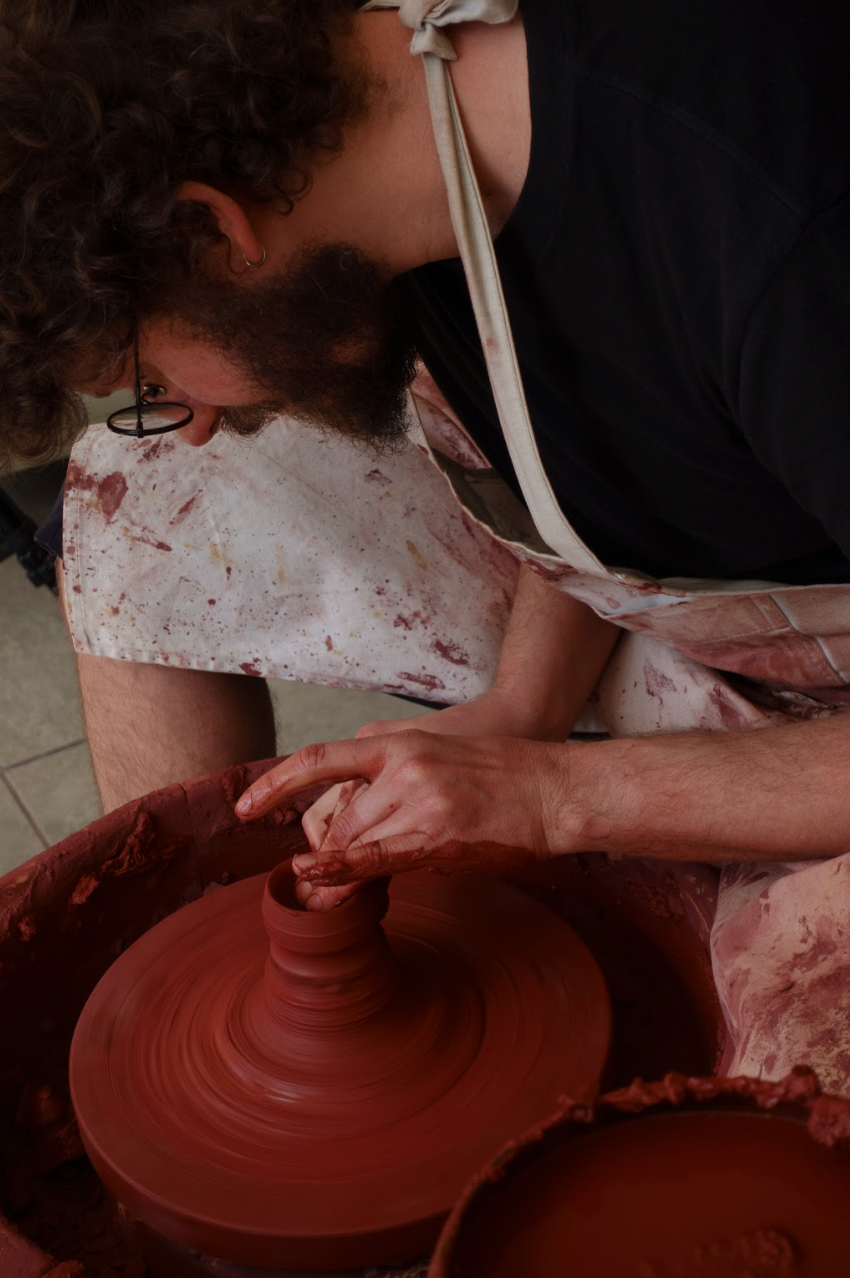 Person working with clay on a potter's wheel in a workshop setting