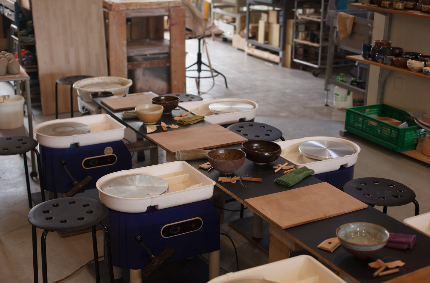 Workshop with pottery wheels, clay items, and tools on a table.