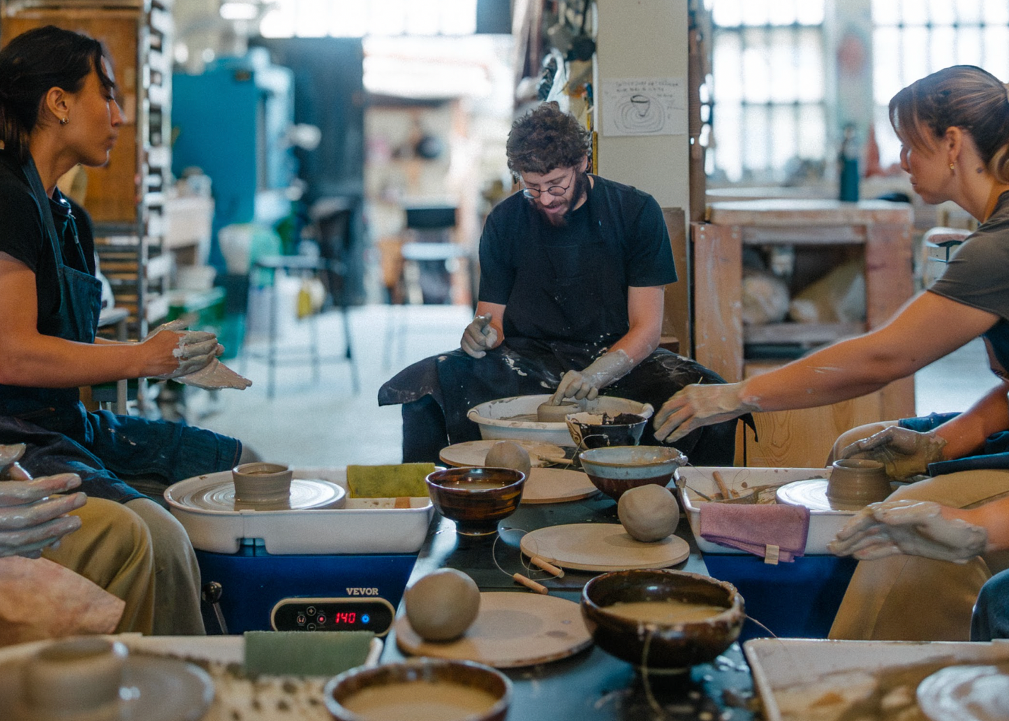 Three people working with clay in a pottery studio.