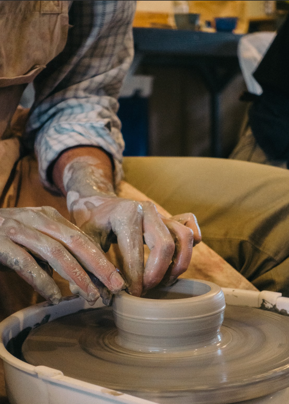 Person working with clay on a pottery wheel in a workshop setting.