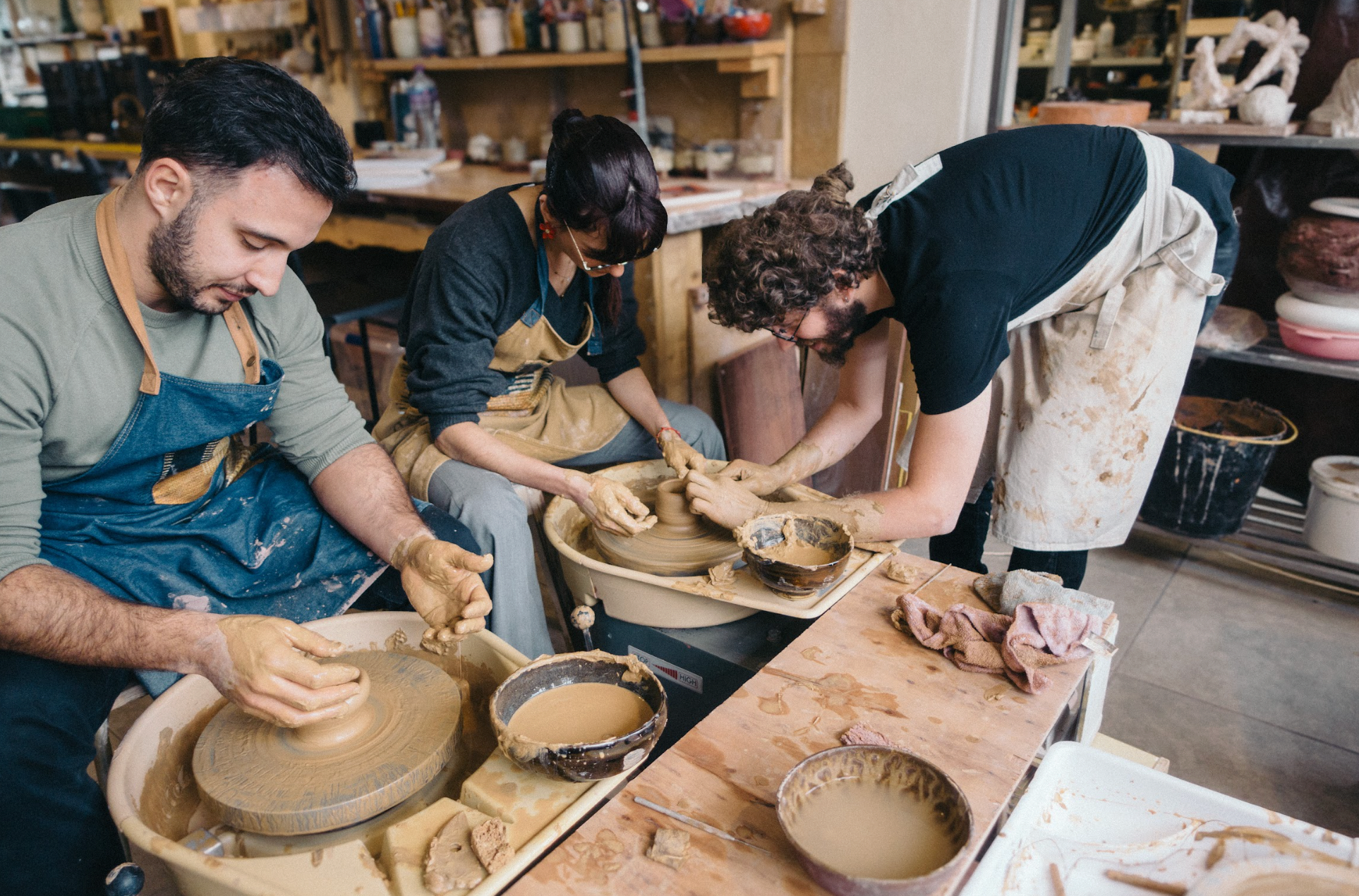 Three potters working on clay pots in a pottery studio.
