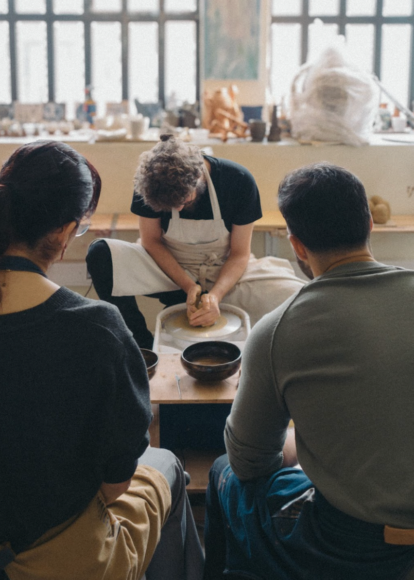 Three people in a pottery studio with one person working on a pot.