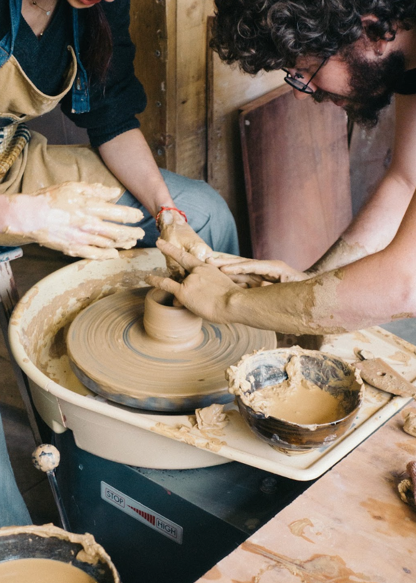 Two people working with clay on a pottery wheel in a workshop.