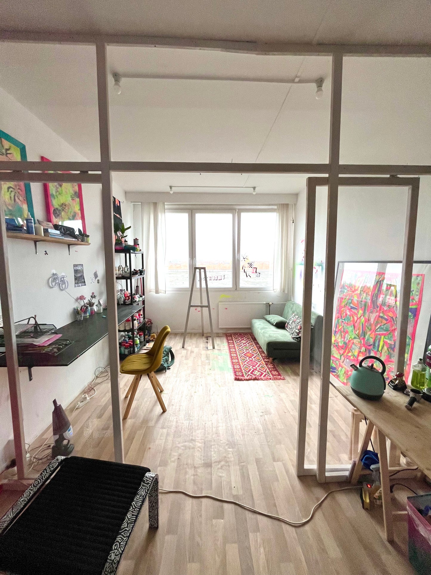 Living room with a desk, shelves, and colorful artwork.