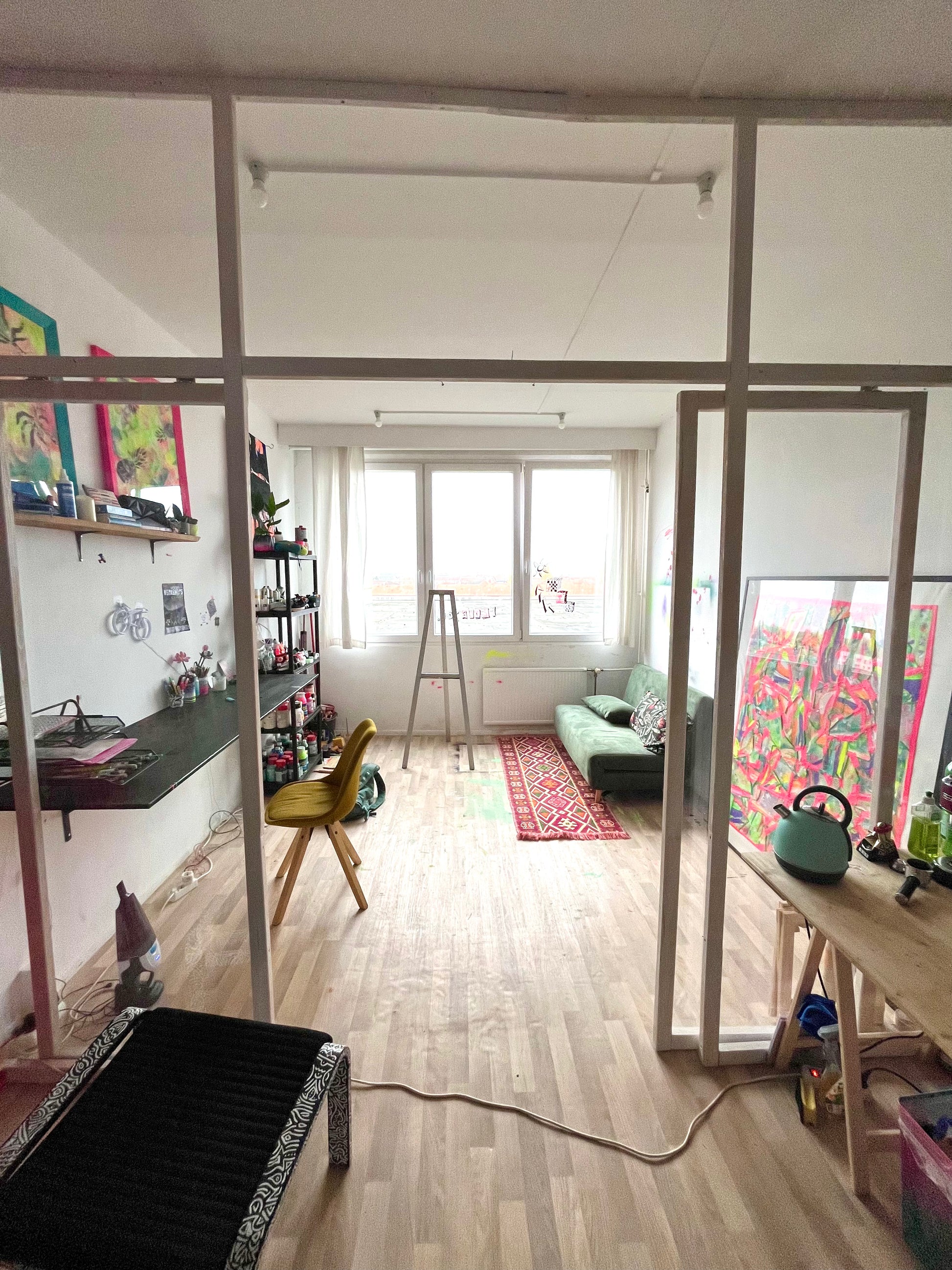 Living room with a desk, shelves, and colorful artwork.