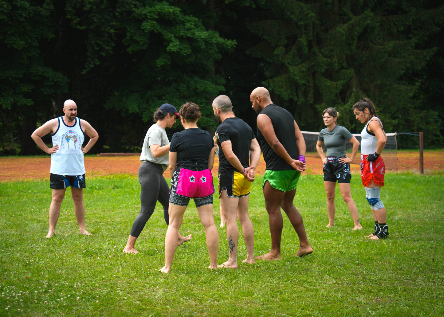 Group of people standing in a circle on grass with trees in the background