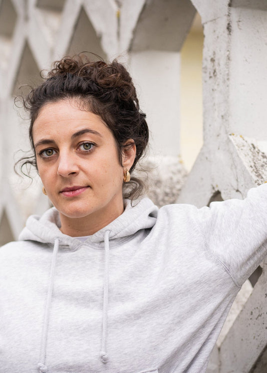 Woman in a gray hoodie leaning against a concrete wall with geometric patterns.