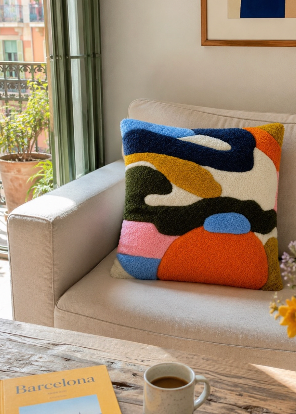 Colorful abstract pillow on a beige sofa with a coffee cup and book in the foreground.