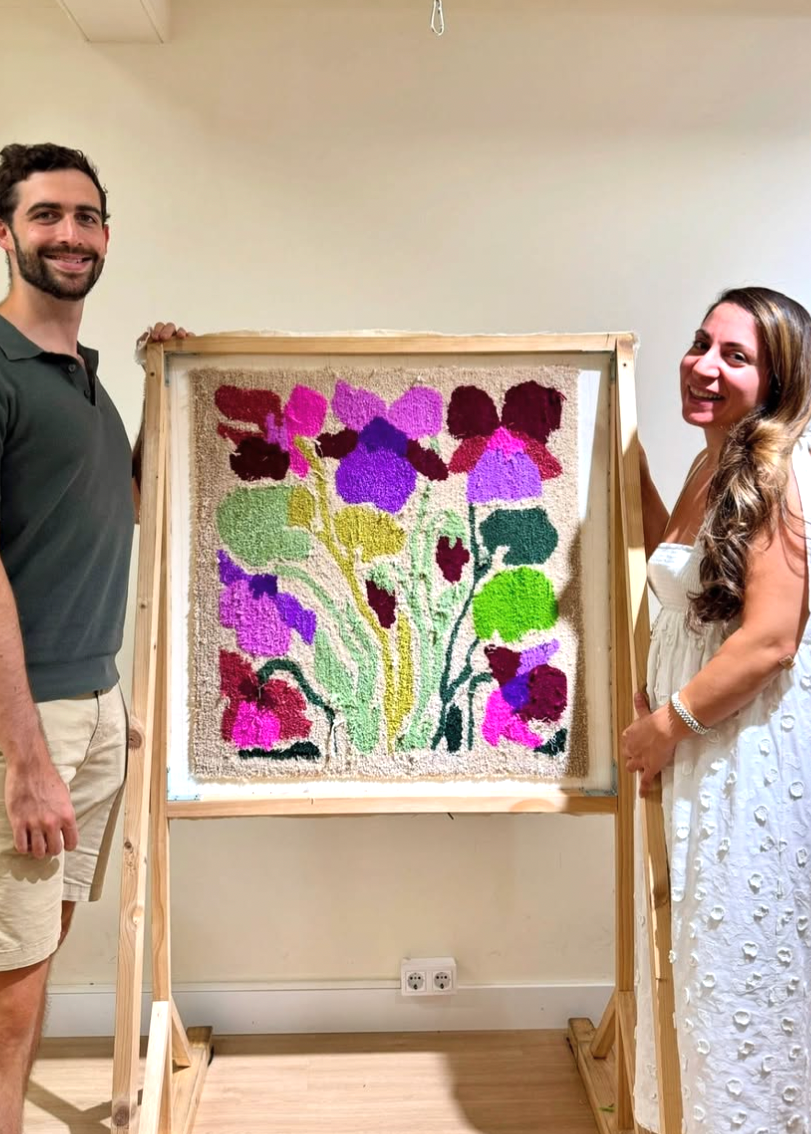 Two people standing next to a framed artwork of colorful flowers on an easel.