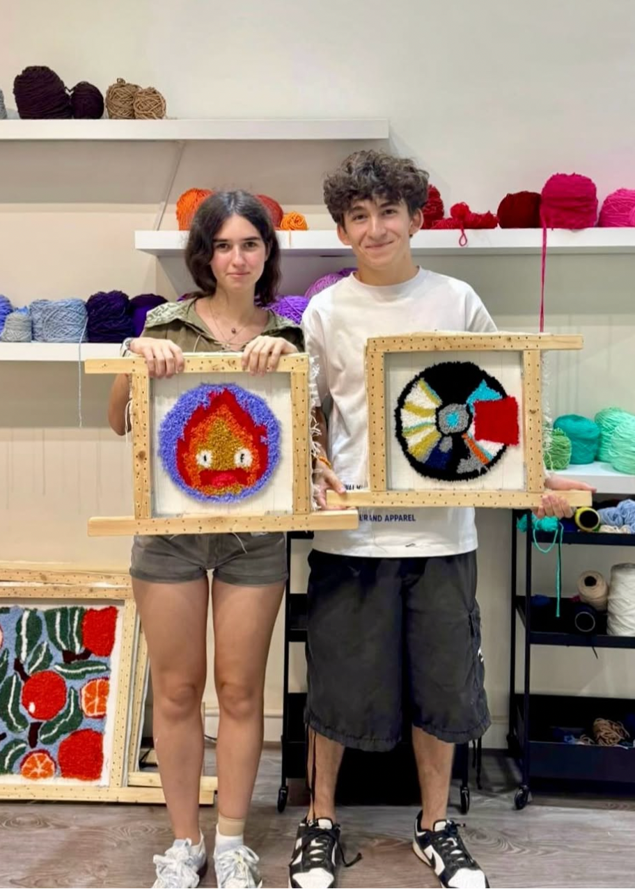 Two people holding framed artworks in a yarn store.