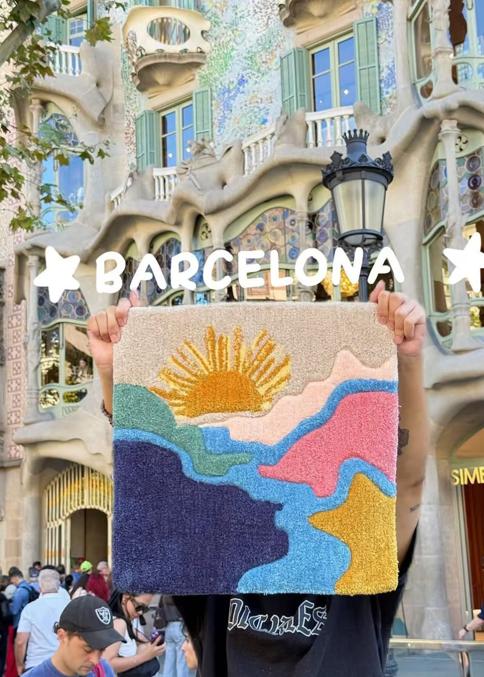 Person holding a colorful rug with a sun design in front of a Barcelona building.