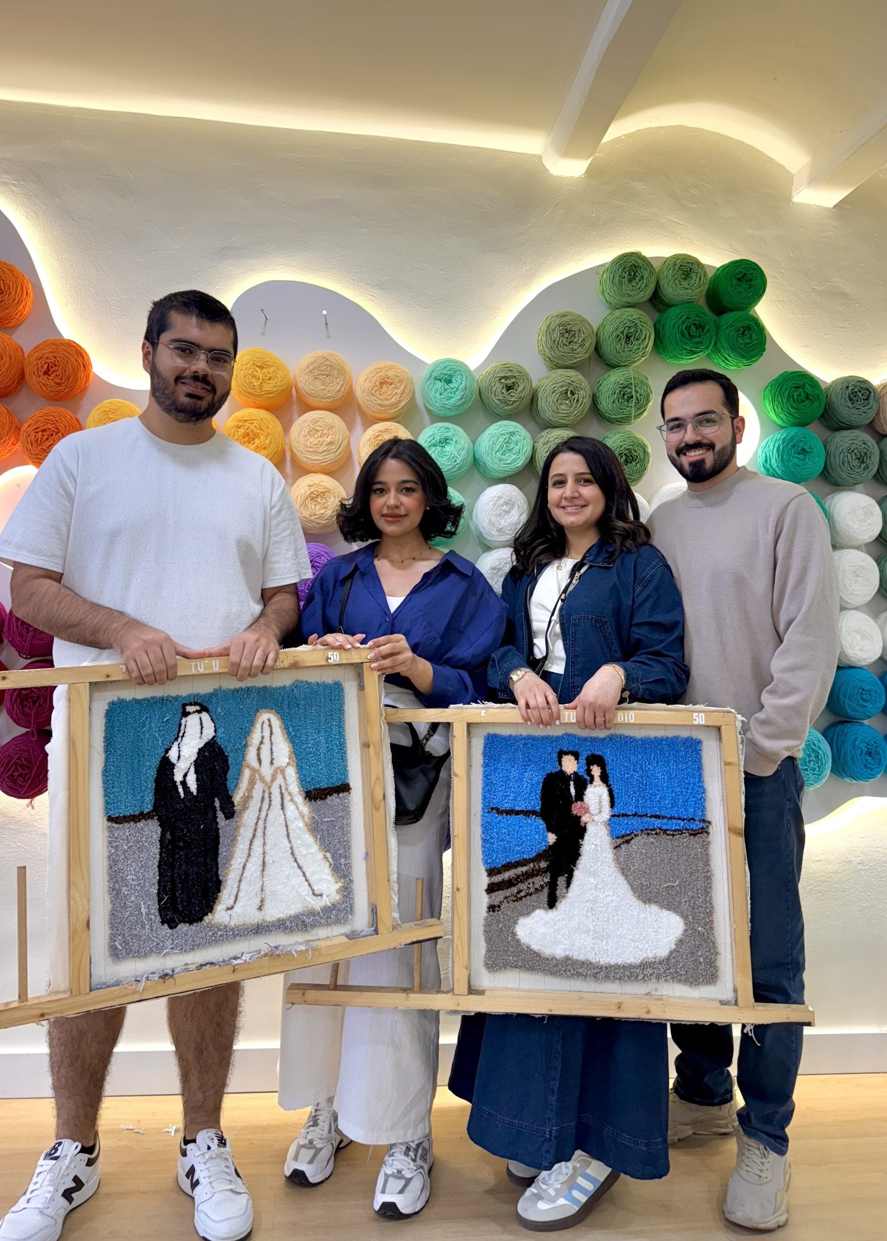 Four people holding artworks of a couple in a colorful room.
