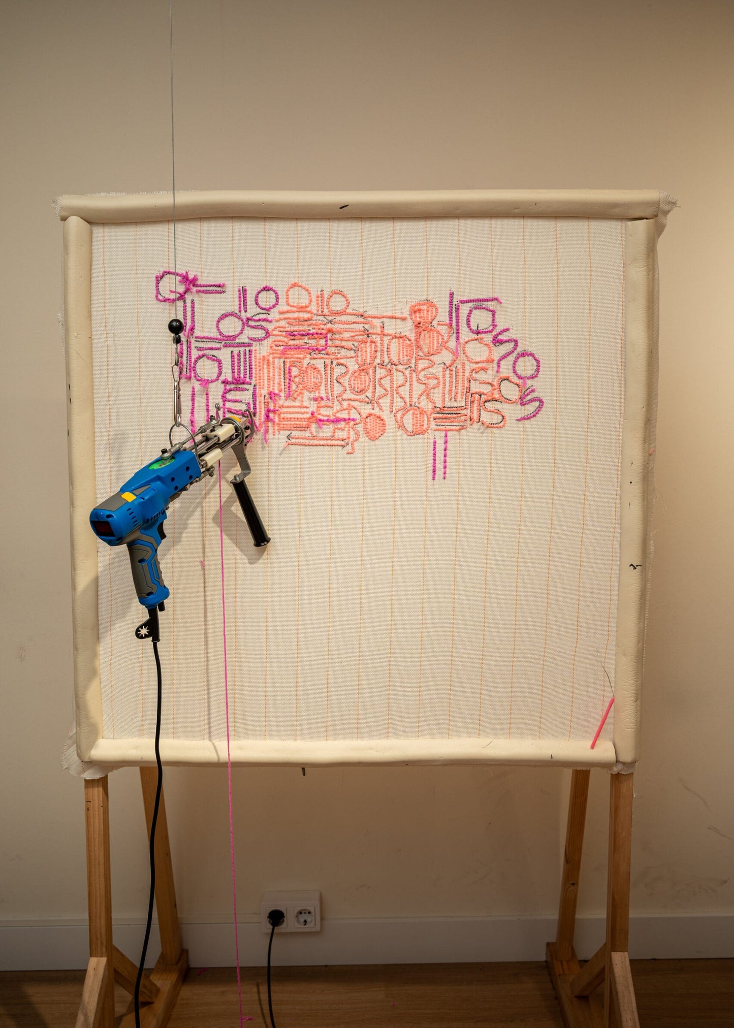 Whiteboard with colorful text and a blue drill on a wooden stand against a plain wall.